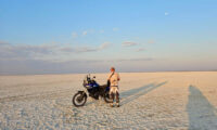 Ein Motorradfahrer auf einem einzelnen Motorrad fährt über die endlos weite, flache Salzpfanne der Makgadikgadi