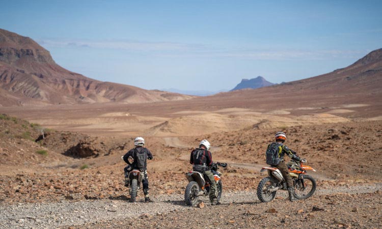 savannenlandschaft-afrika Drei Motorradfahrer ziehen ihre Spuren durch sanfte Hügellandschaft, die sich scheinbar endlos in die Ferne erstreckt. Ein Sinnbild für Weite